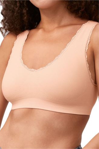 Woman wearing a soft peach Amoena seamless mastectomy bra with scalloped edges, shown from the chest up