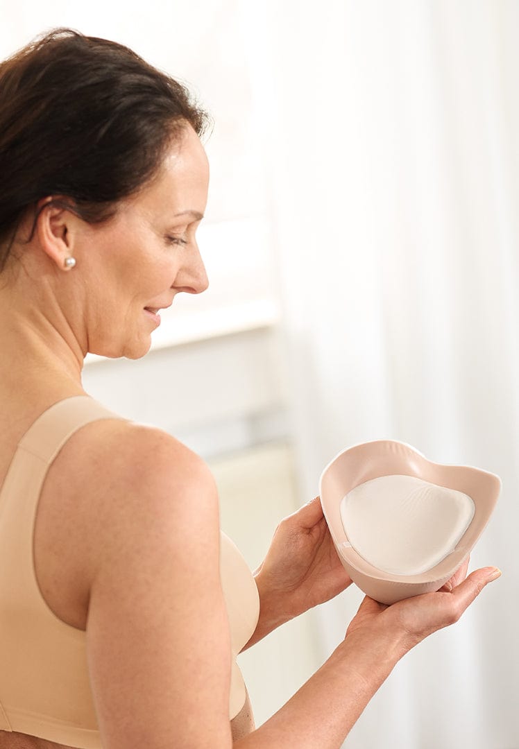 Woman holding a custom breast forml against a light background